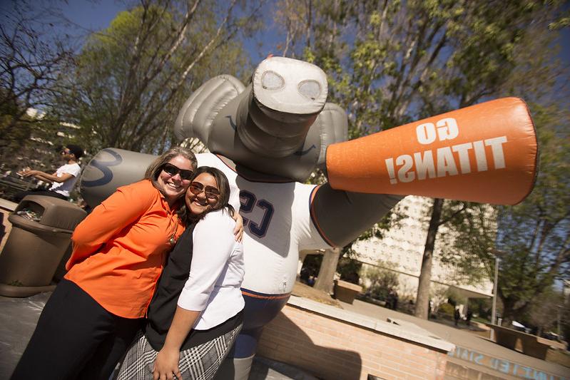 Two staff members pose in front of Tuffy Titan inflatable that has an airhorn saying "GO TITANS!".